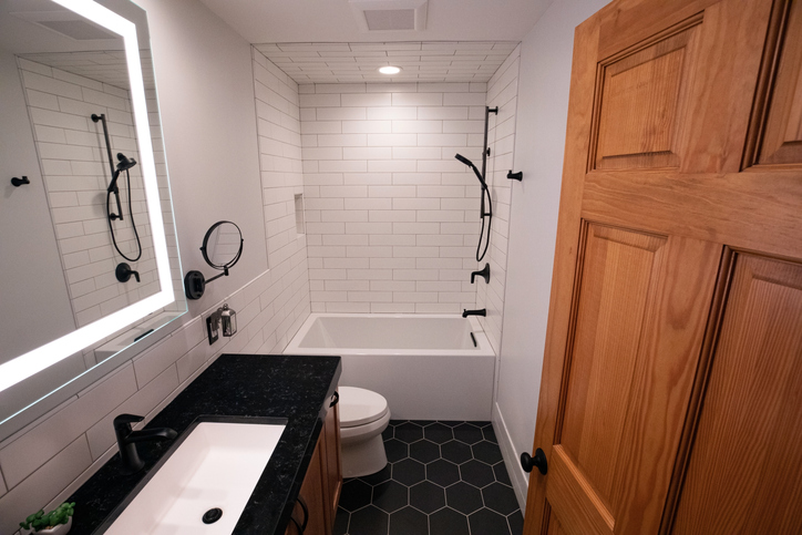 Modern bathroom design with matte black floor, matte black fixtures and deep soaking tub with lighted mirror.